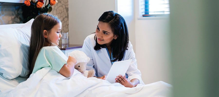 Female caregiver reading to child patient in hospital bed